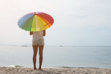 Young woman holding rainbow umbrella and happy on the beach.