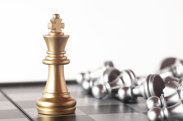 Gold king on a chess board surrounded by a number of fallen silver chess pieces with selective focus
