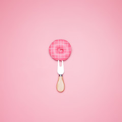 Top view of a pink donut on a fork on a pastel pink background. Minimal design.