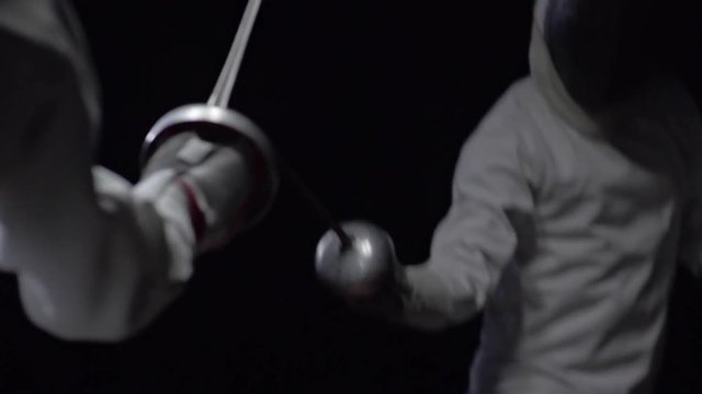 Slow motion of two fencers in protective gear fighting with foils in dark studio