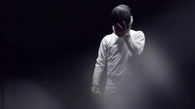 Tracking slow motion footage of young handsome fencer taking off protective mask. Studio shot 