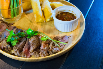 Sliced grilled beef steak with green leaves salad on rustic plate with cutlery. Medium rare barbecue steak and healthy salad on gray stone background, top view, place for text