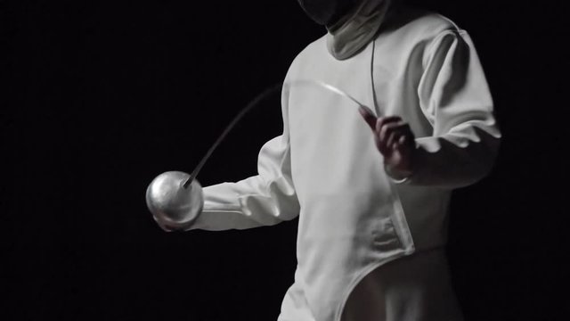 Tilt up of professional fencer bending blade of sword while preparing for fighting. Slow motion studio shot