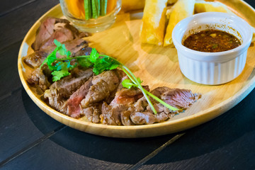 Sliced grilled beef steak with green leaves salad on rustic plate with cutlery. Medium rare barbecue steak and healthy salad on gray stone background, top view, place for text
