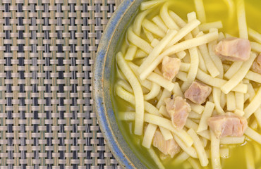 Top close view of chicken noodle soup in an old stoneware bowl atop a woven plastic place mat.