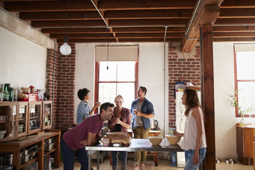 Five friends stand talking over coffee in a kitchen