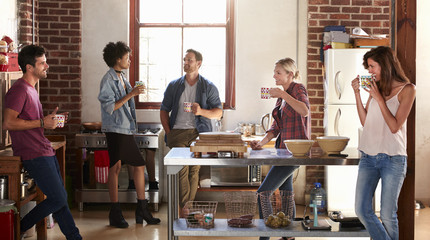 Five friends stand hanging out in kitchen, quarter length