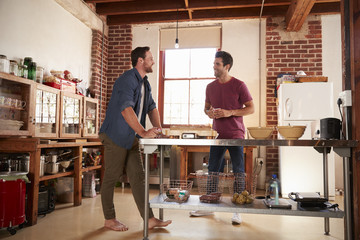 Two male friends hanging out in kitchen, full length