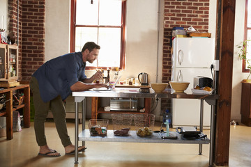 Young man shopping on-line in kitchen, full length side view