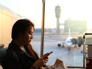 unhappy woman who wearing glasses is using smart phone while waiting for delayed flight