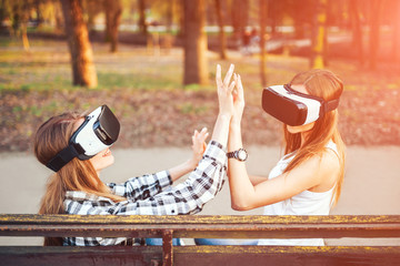 Two pretty girls enjoy virtual reality glasses outdoor
