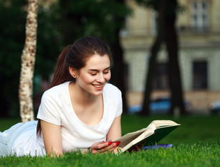 Happy girl student in city park reading a book
