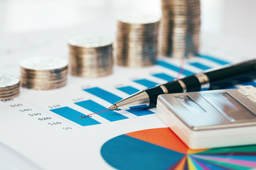 Stack of coin with financial chart, pen and calculator