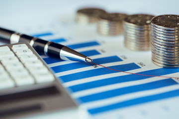 Stack of coins with bar chart, pen and calculator