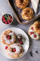 Filling and empty homemade choux pastry cake Paris Brest with raspberries, almond, sugar powder, rosemary on plate and oven tray with berries over gray texture background. French dessert. Flat lay