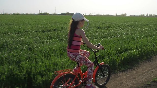 Child on a bicycle. Little girl on a bicycle in the countryside. The girl is riding a bicycle on a country road. Slow motion.