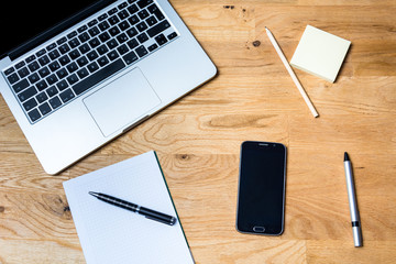 Work desk from above with laptop, smartphone, notepad and other accessories on wooden table