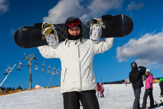 Young male in ski-suit standing and holding his snowboard on his shoulders
