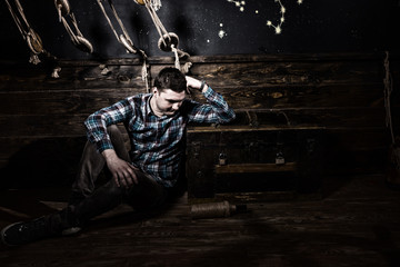 Sad guy sits near a chest, holding glass bottle and trying to get out of the trap in a ship