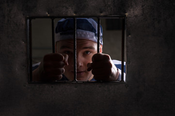 View through iron door with prison bars on male prisoner holding bars in a jail cell