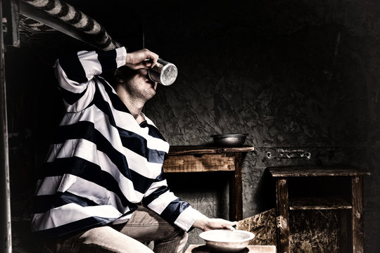 Male prisoner drinking from an aluminum cup in a prison cell