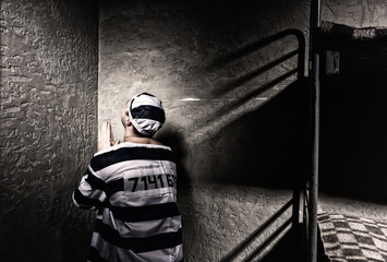 Male prisoner is sitting in the corner and praying in a small prison cell