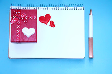 A gift box, hearts, a notebook and pen on a blue background 