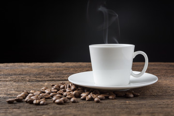 Coffee cup and beans on wooden table. Dark background