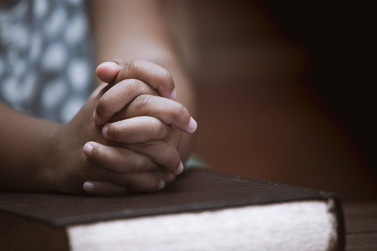 Little girl hands folded in prayer on a Holy Bible in church  for faith concept in vintage color tone