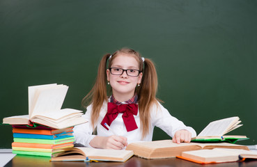 Young girl with books near empty green chalkboard