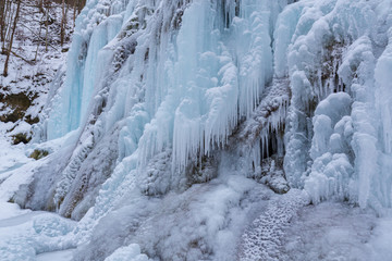 Fototapeta na wymiar Wild river, beautiful frozen waterfalls and fresh snow in a mountain forest, on a cold winter day