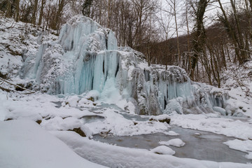 Wild river, beautiful frozen waterfalls and fresh snow in a mountain forest, on a cold winter day