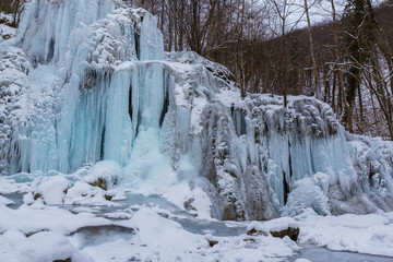 Fototapeta na wymiar Wild river, beautiful frozen waterfalls and fresh snow in a mountain forest, on a cold winter day