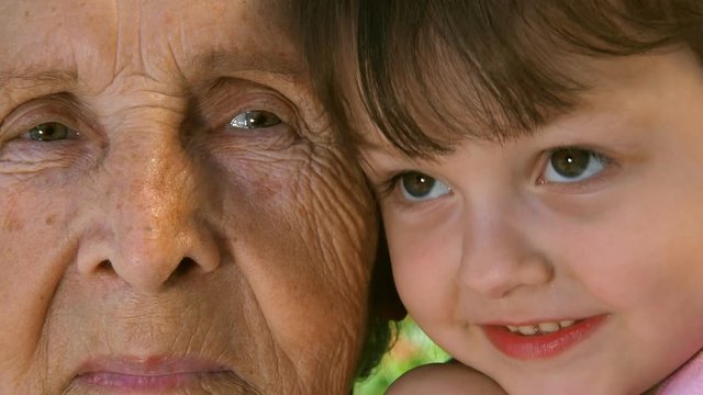 Grandmother with granddaughter. Portrait of an elderly woman and a child. The face of an elderly woman and a child. Grandmother with grandson close-up. Elderly and younger eyes. Two faces close-up.
