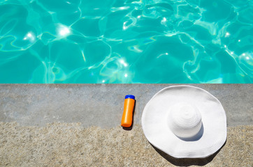 Summer hat and sunscreen near the pool