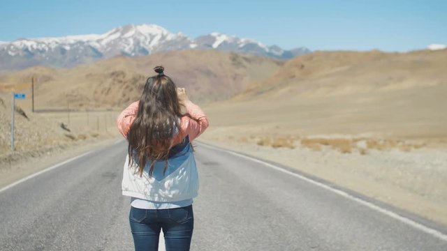 Young attractive tourist woman is taking photos on road with mountains at background