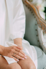 bride in a robe sits on the bed with her hands clasped, on the finger of the bride the wedding ring