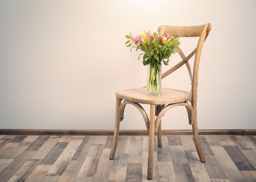 Chair and vase with bouquet of beautiful tulips on white wall background