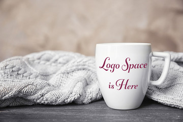 White cup and knitted scarf on grey table