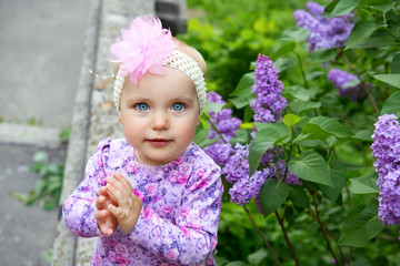 Beautiful little girl happy smiling and claps her hands over lilac flowers in spring park. Childhood. Cute kid's face over nature background. Cheerful child's portrait, soft focus.