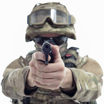Military man in camouflage uniform, armor vest, dark glasses and helmet with gun aiming at the enemy