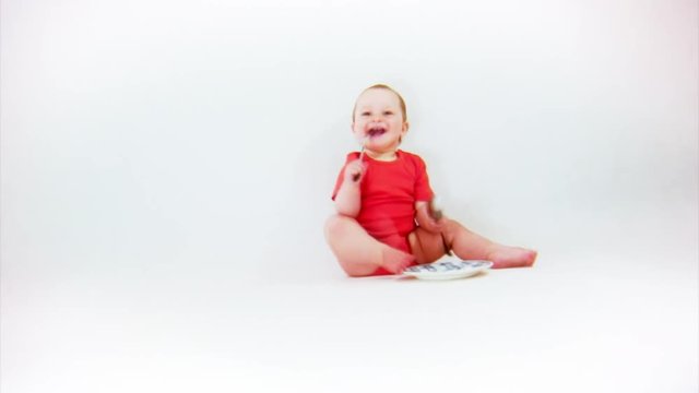 Baby in red body playing with fork, spoon and a plate on a white background.