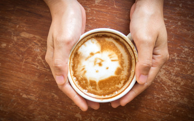 Woman hands holding cup of coffee. Top view. Cute latte art, cat paint. With dark vignette.