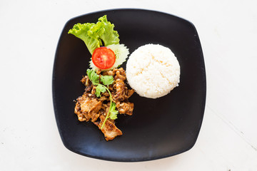 Sliced pork fried served with rice. On black plate over white table. Top view.