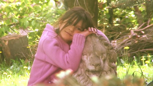 Small girl by a stone lion in the garden.