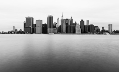 Manhattan skyline in cloudy day, New York skyscrapers reflected in water, black and white photo, USA