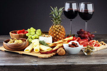 Italian antipasti wine snacks set. Cheese variety, Mediterranean olives, pickles, Prosciutto di Parma with grapes, wine in glasses over black grunge background