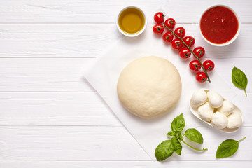 Fototapeta na wymiar Raw pizza dough with baking recipe ingredients: mozzarella, tomatoes sauce, basil, olive oil, cheese, spices. Italian margherita on wooden table. Italian pizza margarita
