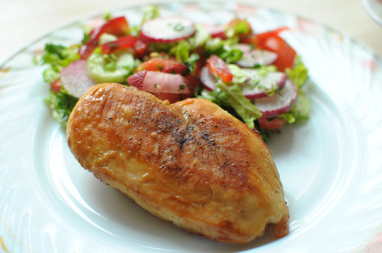 Baked chicken breast with vegetable salad on a white plate