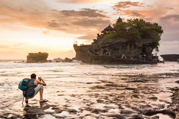 Traveler Man taking photo of beautiful tanah lot landscape during sunset, Ancient hinduism temple...
